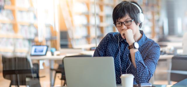 Person sitting at table with headphones on, typing on computer.